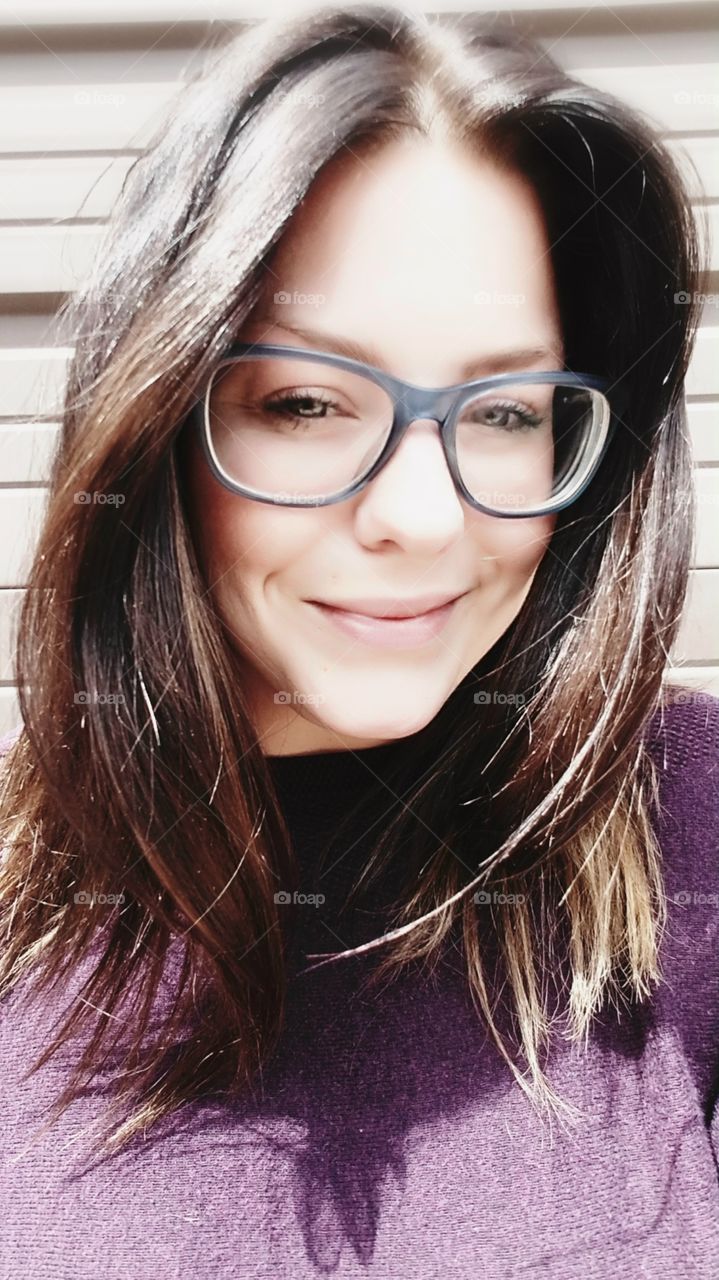 Smiling woman with a fresh face and light to dark brown hair. Blue eye glasses.