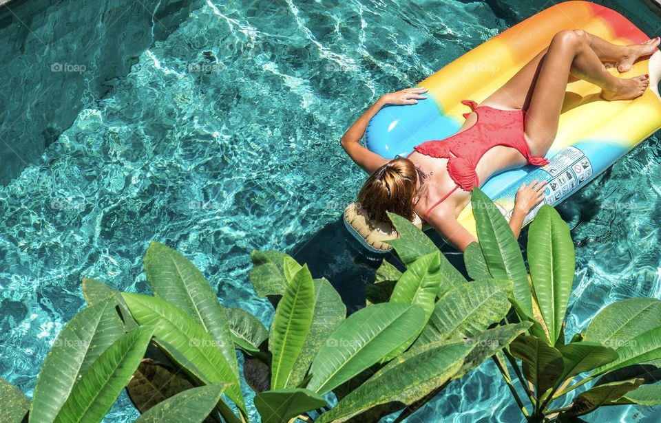 Girl sunbathes in the pool on a bright mattress 