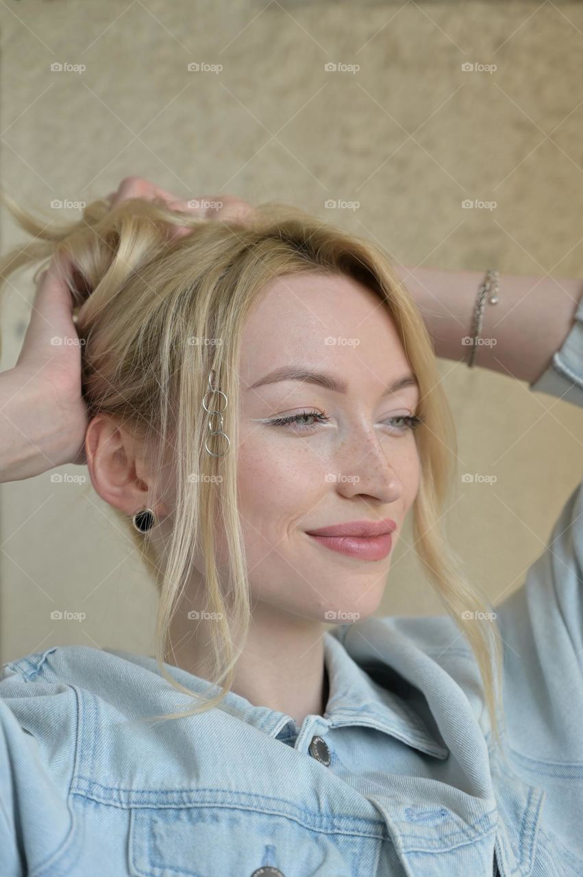 Portrait of a cute girl with blond hair with a beautiful look with her hands near her head