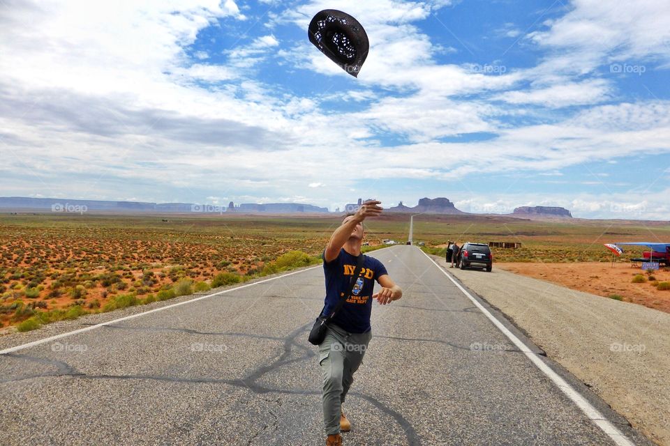 A Man plays with his hat on the famous road called I163 that through the Monument valley tribal park,Utah