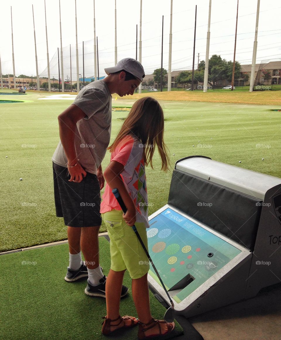 You have to do what?. Brother helping sister with her game at Top Golf
