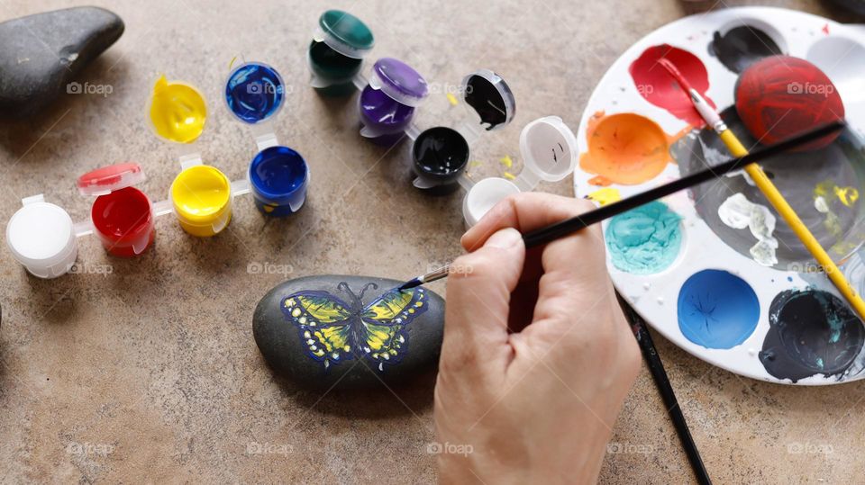 hand painting a butterfly on small rock