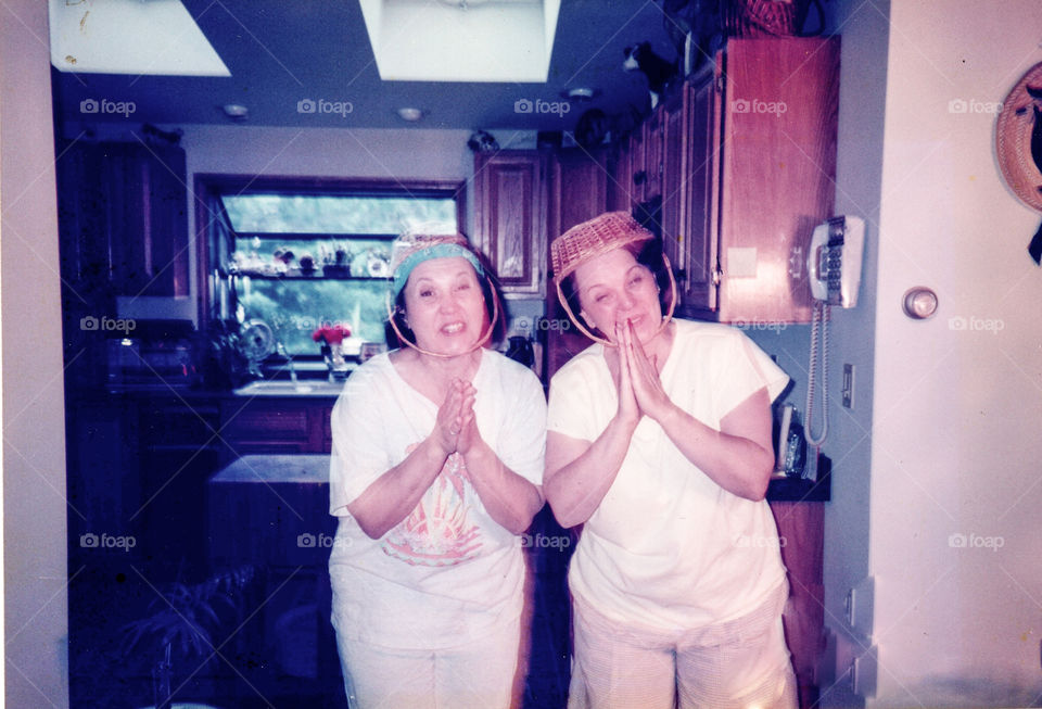Two women/girls acting silly with baskets on their heads, posing for the camera. Girls being silly, funny girls! Smiling at camera with hands folded!