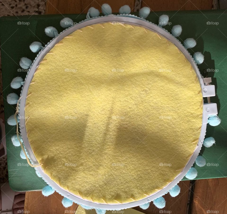 Finished backside of pastel hand embroidered giraffe and floral baby gift with pom pom border. Yellow, hand stitched felt backing. 