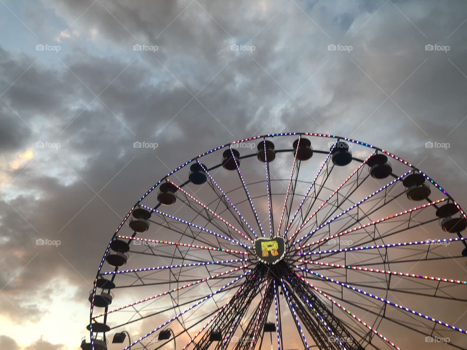 A wide angle shot of a beautiful Ferris wheel, standing dominant over the imposing clouds in the background. 