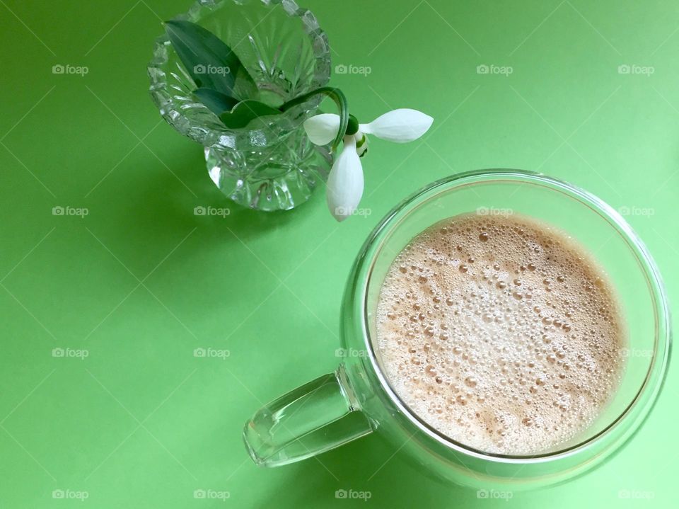 Coffee cup and snowdrop on green background