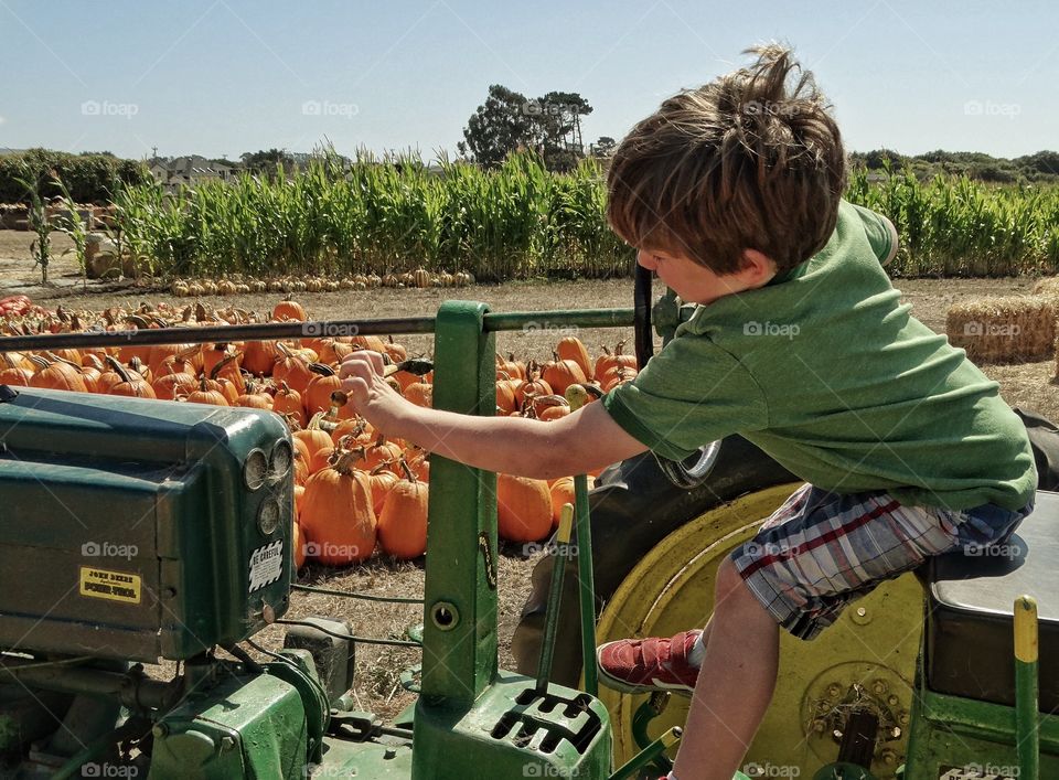 American Farm Boy. Boy Riding A John Deere Tractor At The Pumpkin Patch
