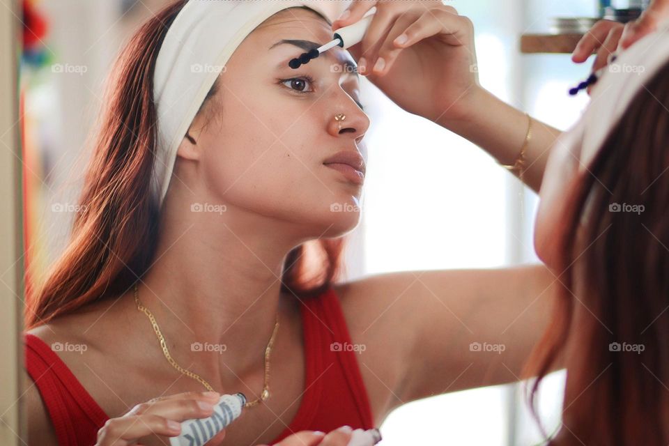 Young pretty woman is using a mascara in front of a mirror