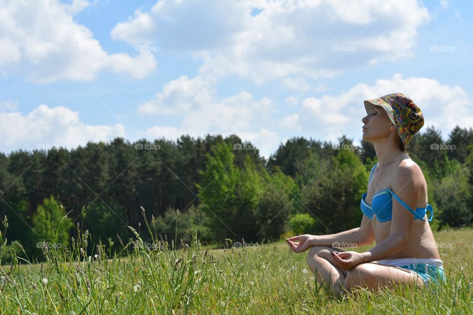 woman training yoga and meditation on a green grass lake shore summer time