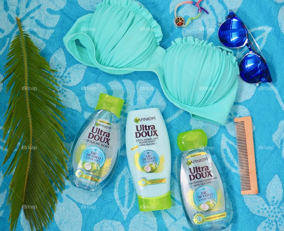 Garnier eau de coco shampoo, conditioner and bath gel on a blue towel with comb and palm leaf and blue sunglasses and bikini.