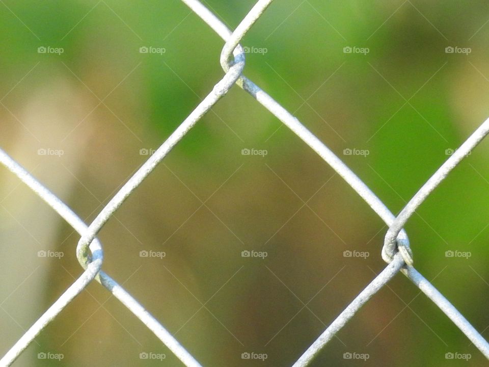 Chain links macro photography seeing a middle Diamond shape from the metal fence with green background from forest.