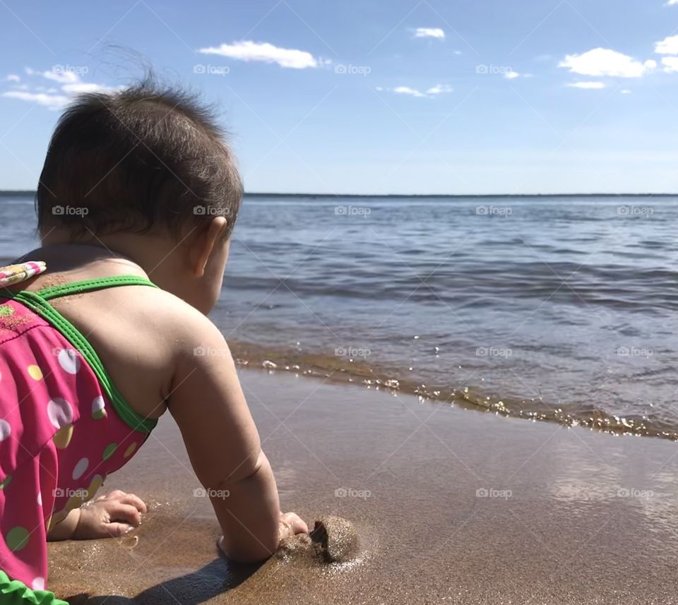 Baby girl playing in the sand at a beach looking out into the water