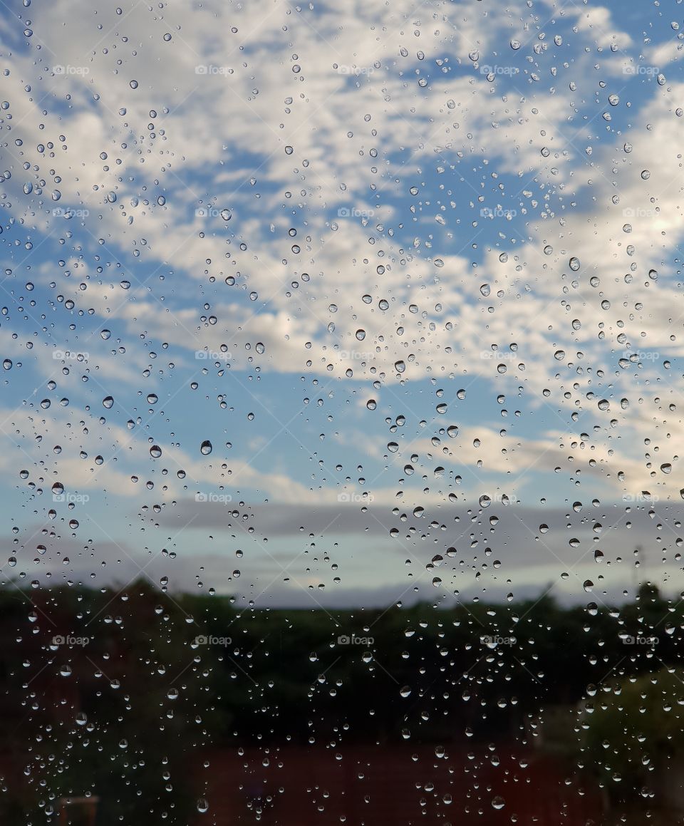 Blue cloudy sky through a rainy window
