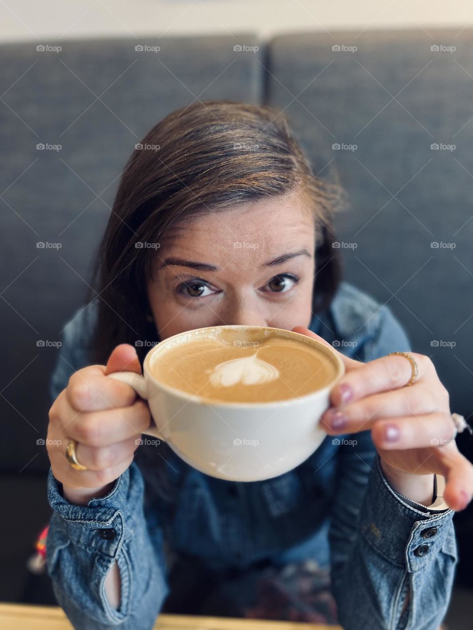 Pretty young women holding a latte with a coffee art heart in a cafe