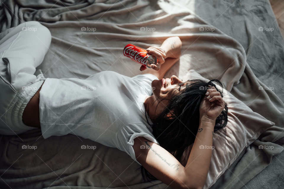 the girl lies on the bed and holds a Coca Cola