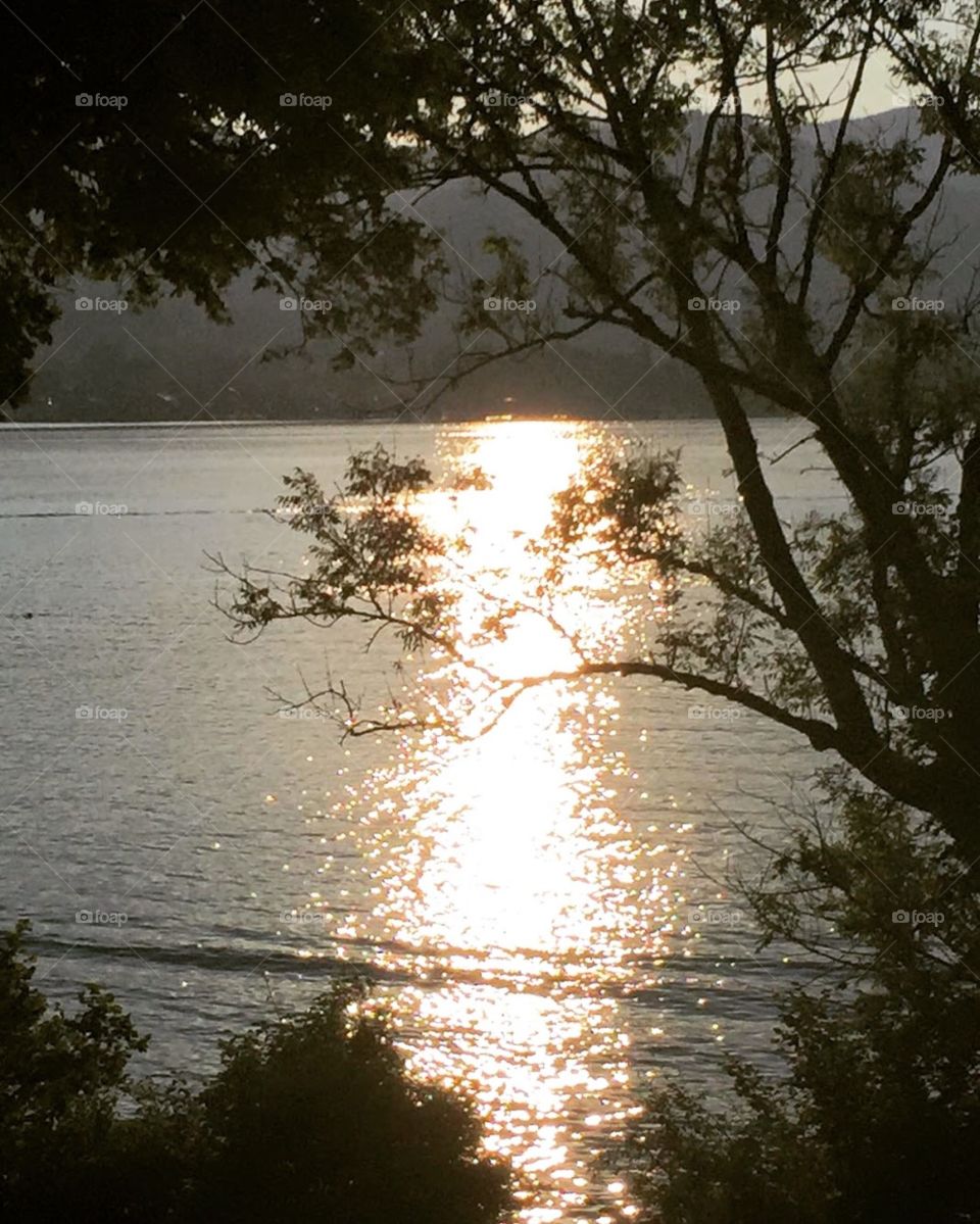 the sun at sunset shines into the lake in a long orange trail, the water is sparkling, the trees had turned dark, the air was cool, and lots of people walking and talking