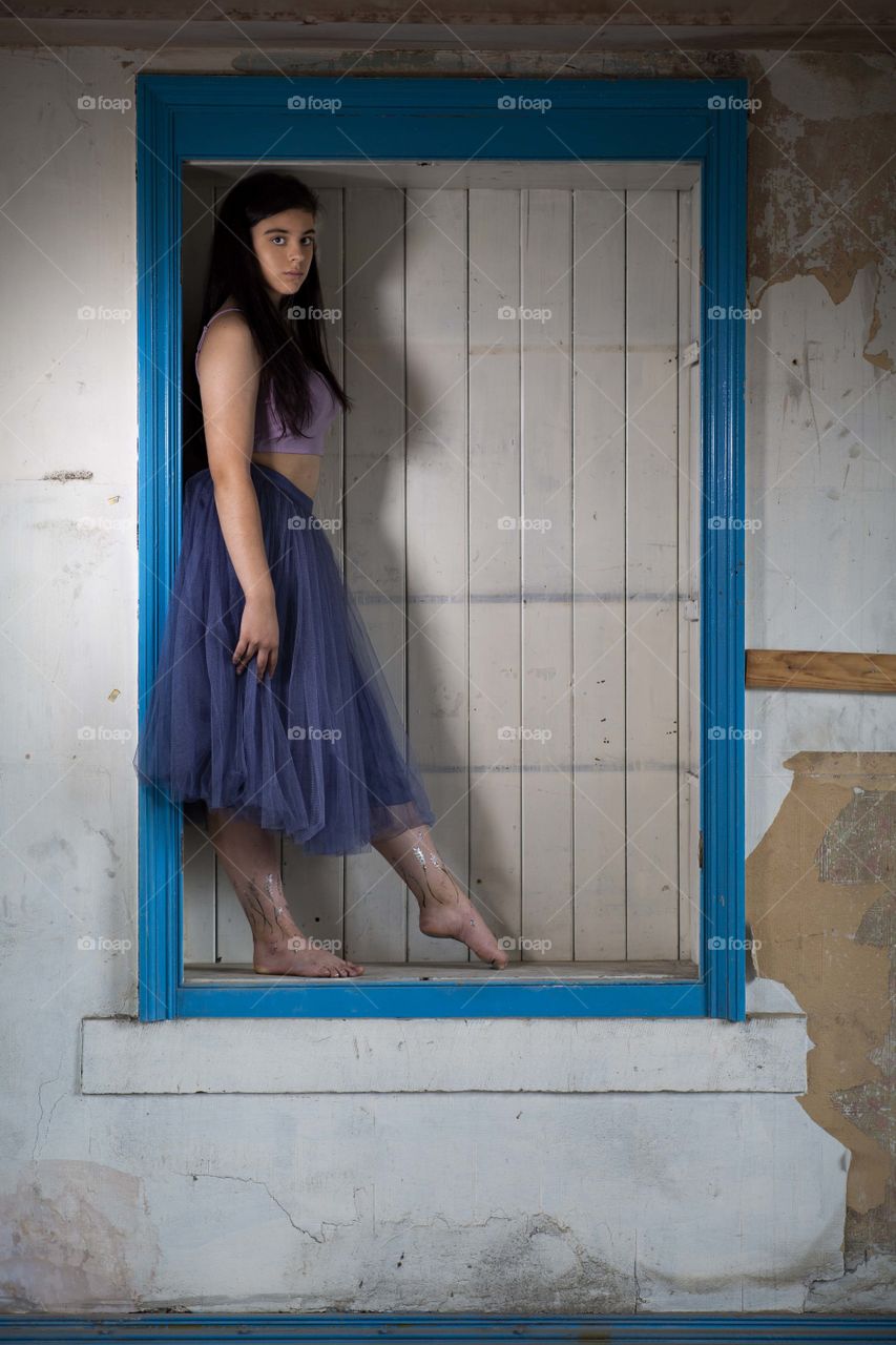 Girl standing in an old cupboard. She is wearing a purple skirt. She is bare footed. She is framed by a blue cupboard frame. 