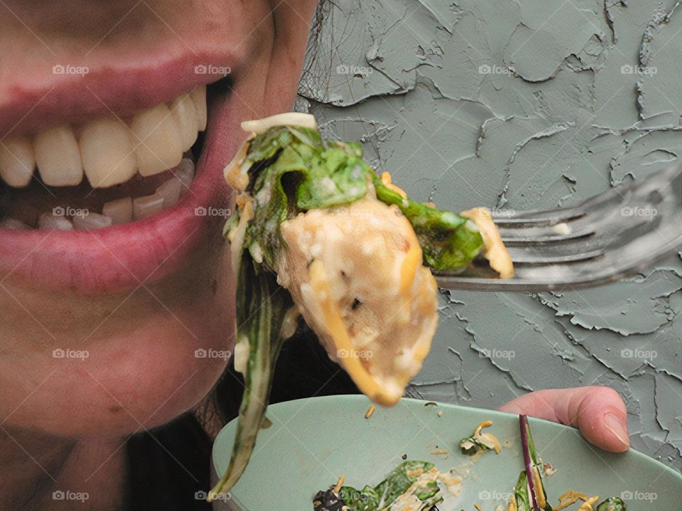 Glimmers close-up of eating a delicious salad with Colby Jack shredded cheese, spring mix lettuce and spinach with parmesan and Italian dressing and mayonnaise on a fork with bowl aside. Mouth opened smiling to eat with hair and grey blue background.