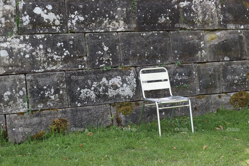 One empty silver chair in meadow in front of stone wall