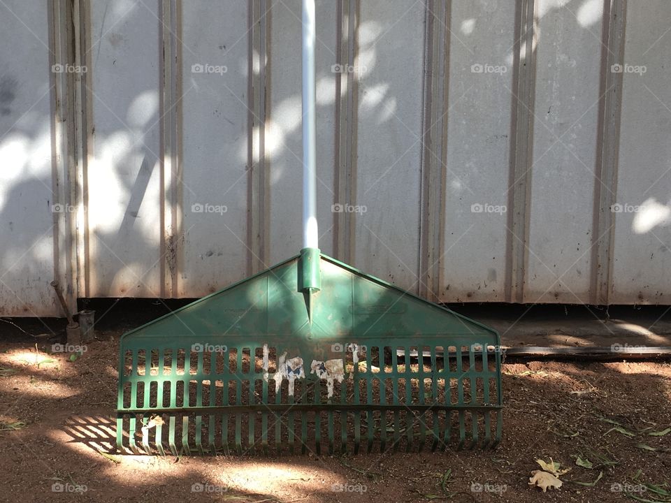 Green rake leaning against outdoor garden shed