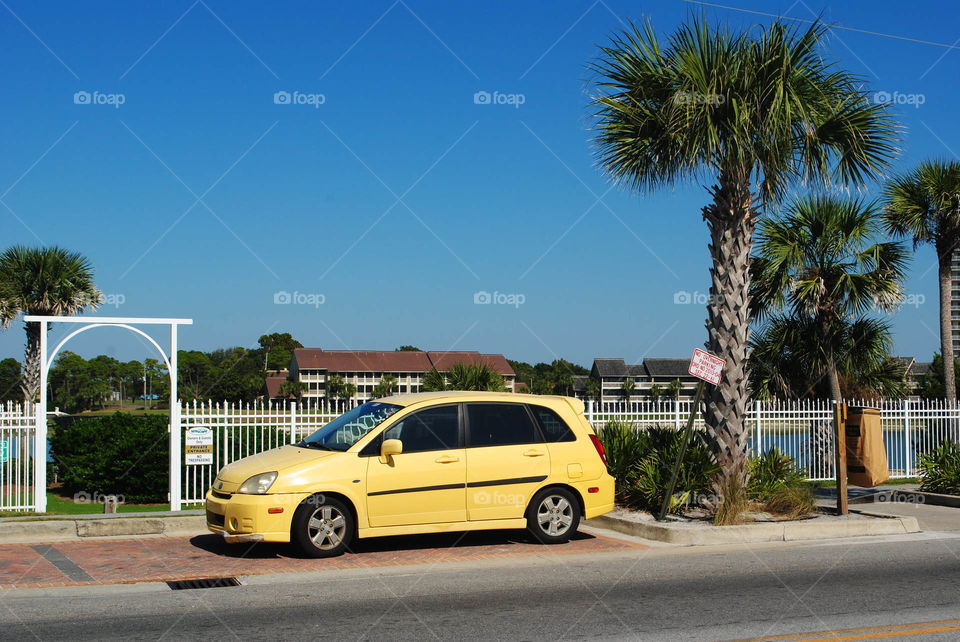 A yellow car parked at the street across the beach