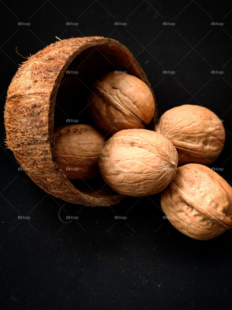 Half a coconut from which walnuts spilled.  Black background