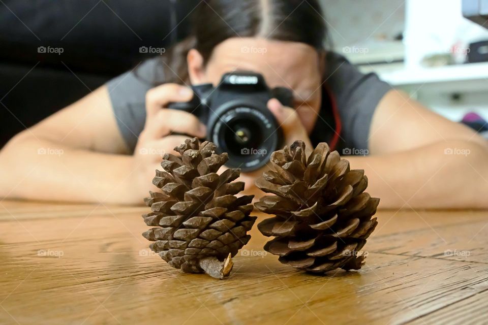 A young woman is laying on the floor and taking a photo of pine cones