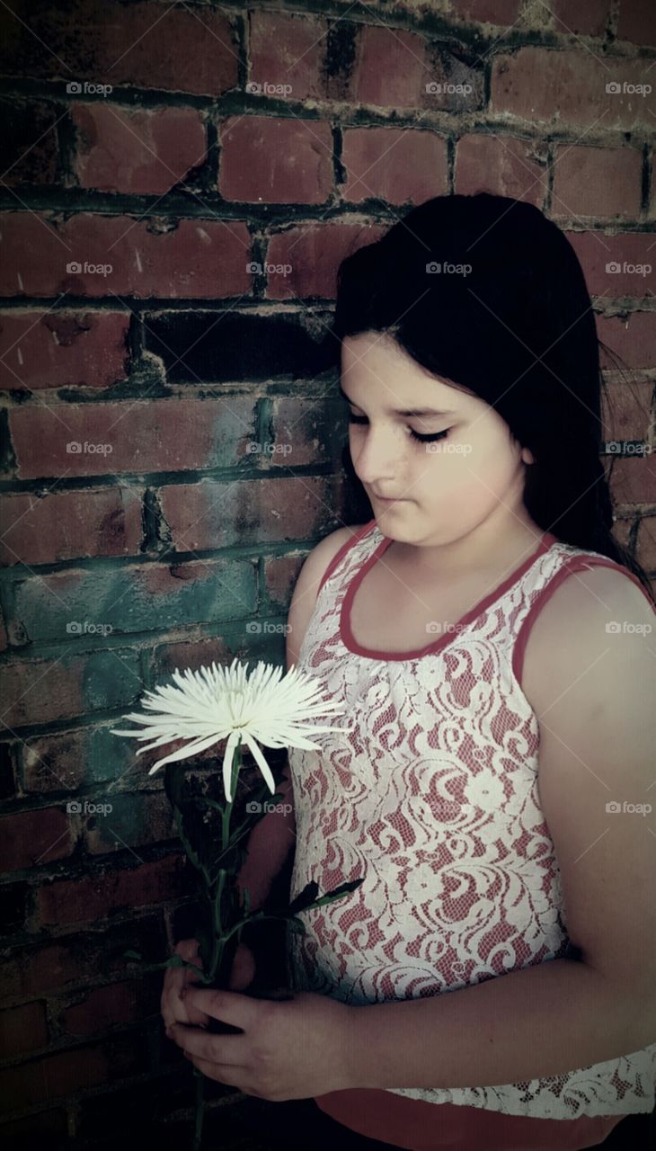 little girl holding flower against brick wall