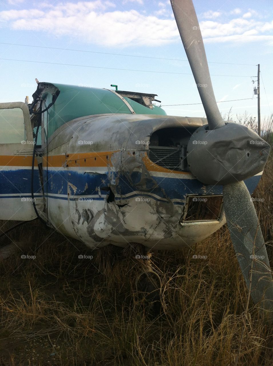 A rugged old airplane. Gold and blue stripes, a real beauty in its day. With dented propeller and cracked windshield, it now sits in a field, remembering its glory days
