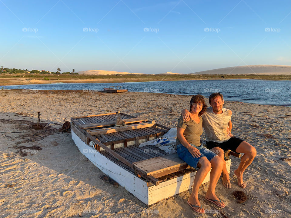 Two Friend sitting on fisher boat in the beach with sea and dunes background 