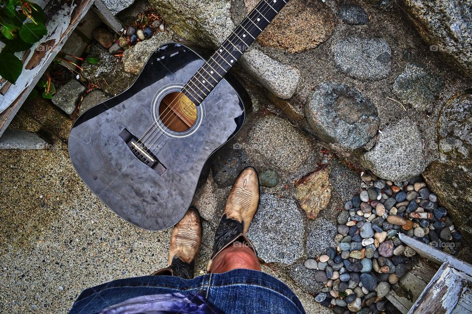 Point of view woman in cowboy boots with black guitar 