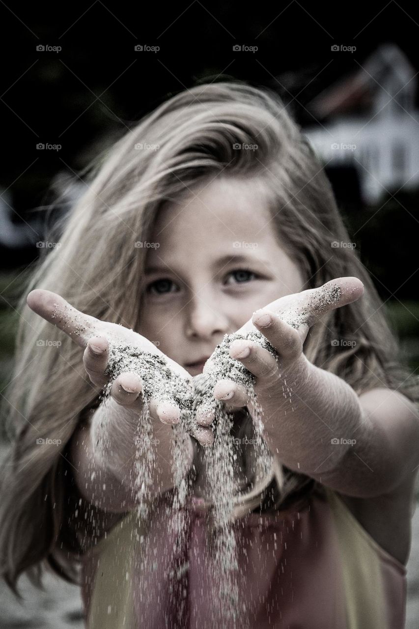 A little girl plays with the beach sand in her hands . Its kinda art at the beach .