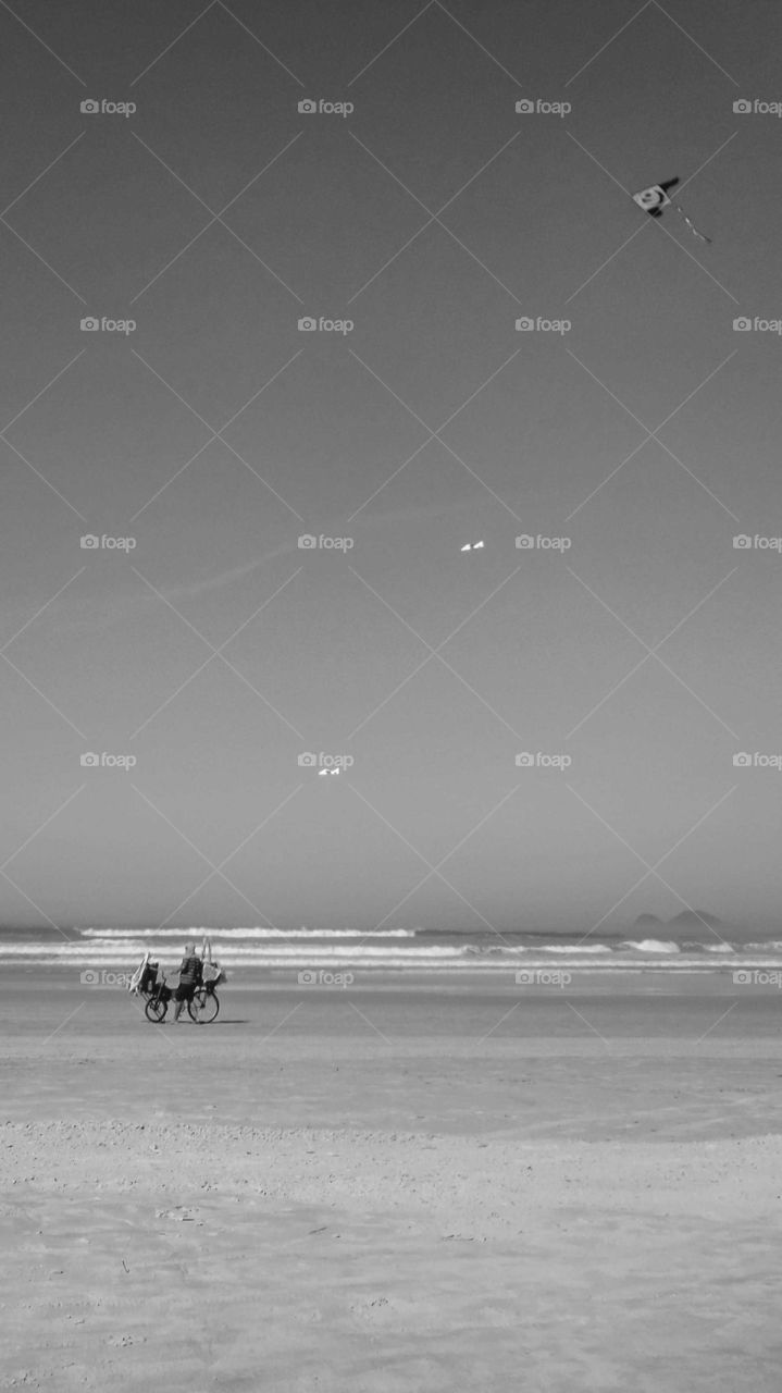 Beautiful Brazilian Beach, at Guarujá's EbsBeautiful Brazilian Beach, at Guarujá's Enseada Beach, sunny day . There's a Man with a cart, a bike, selling kieada Beach, sunny day . There's a Man with a cart, a bike, selling kites. Black and white shot.