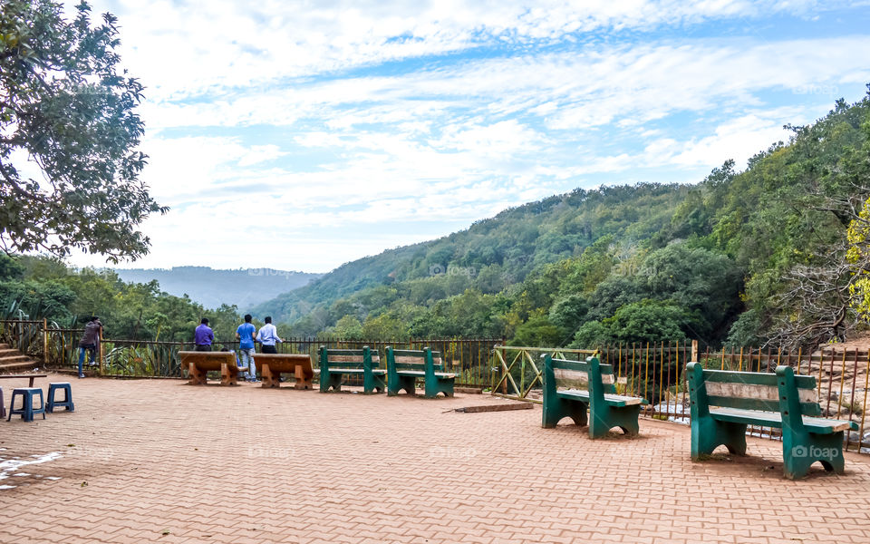 A beautiful lawn with park bench to sit and rest alone on a paved walk with lush greenery surrounded by Satpura and Vindhya mountain ranges in the background. View of Amarkantak Madhya Pradesh, India