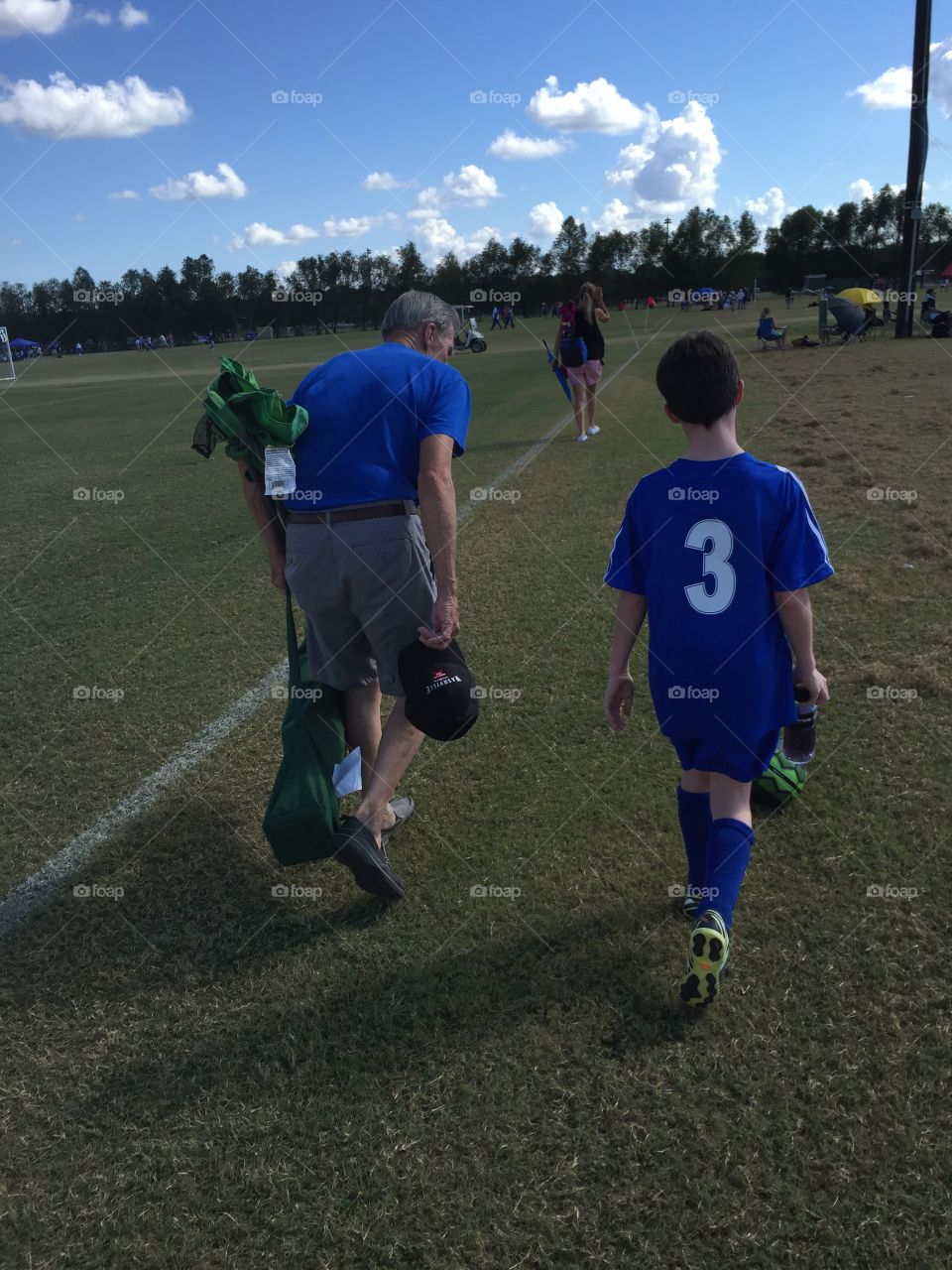 Grandfather carrying soccer gear with grandson walking off the soccer field together on a fall day.