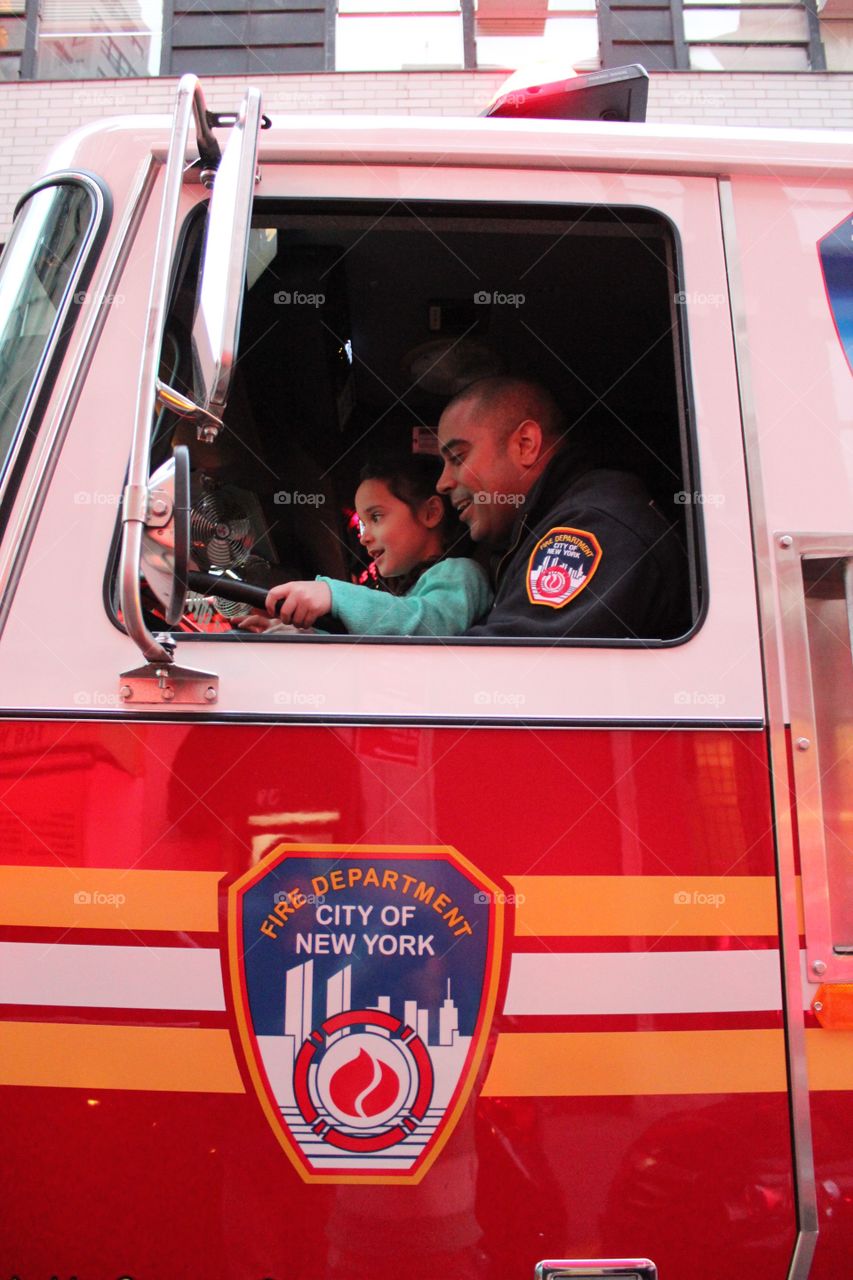 Firefighter sitting with his daughter on driving seat of fire truck