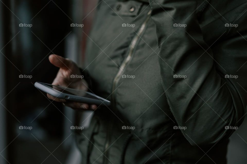 A young girl in a dark green park holds a mobile phone in her hand reading messages in it, standing indoors on a blurred background, close-up side view. The concept of using technology.