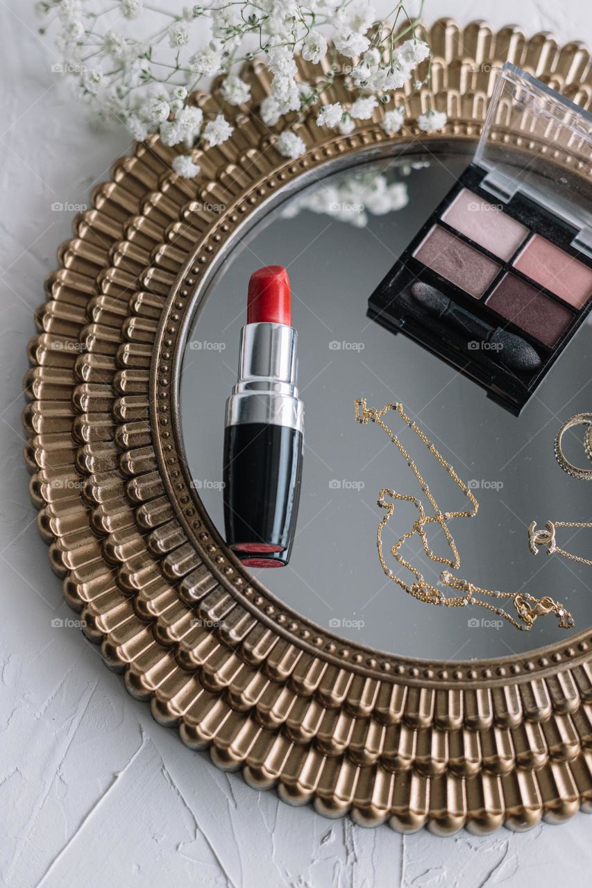 Gold jewellery, Red lipstick and eyeshadow makeup palette.