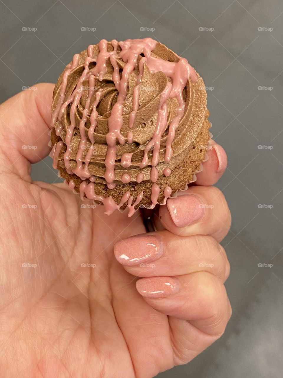 Hand with pink manicure holding a brown sweet 