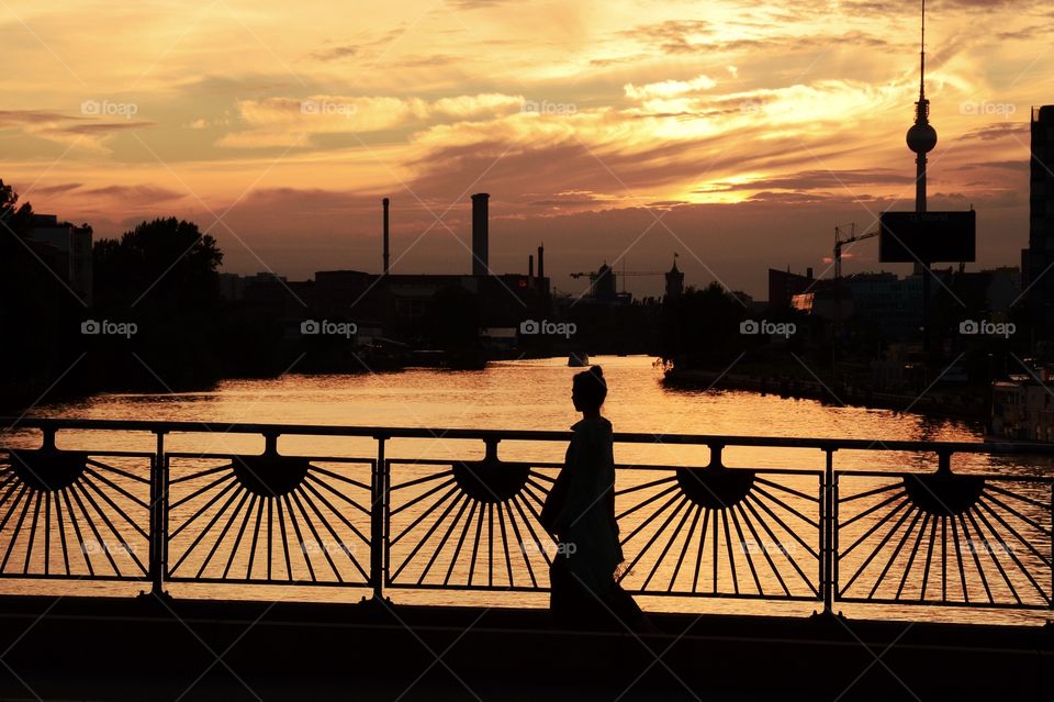 Silhouette of a woman walking on a bridge at sunset