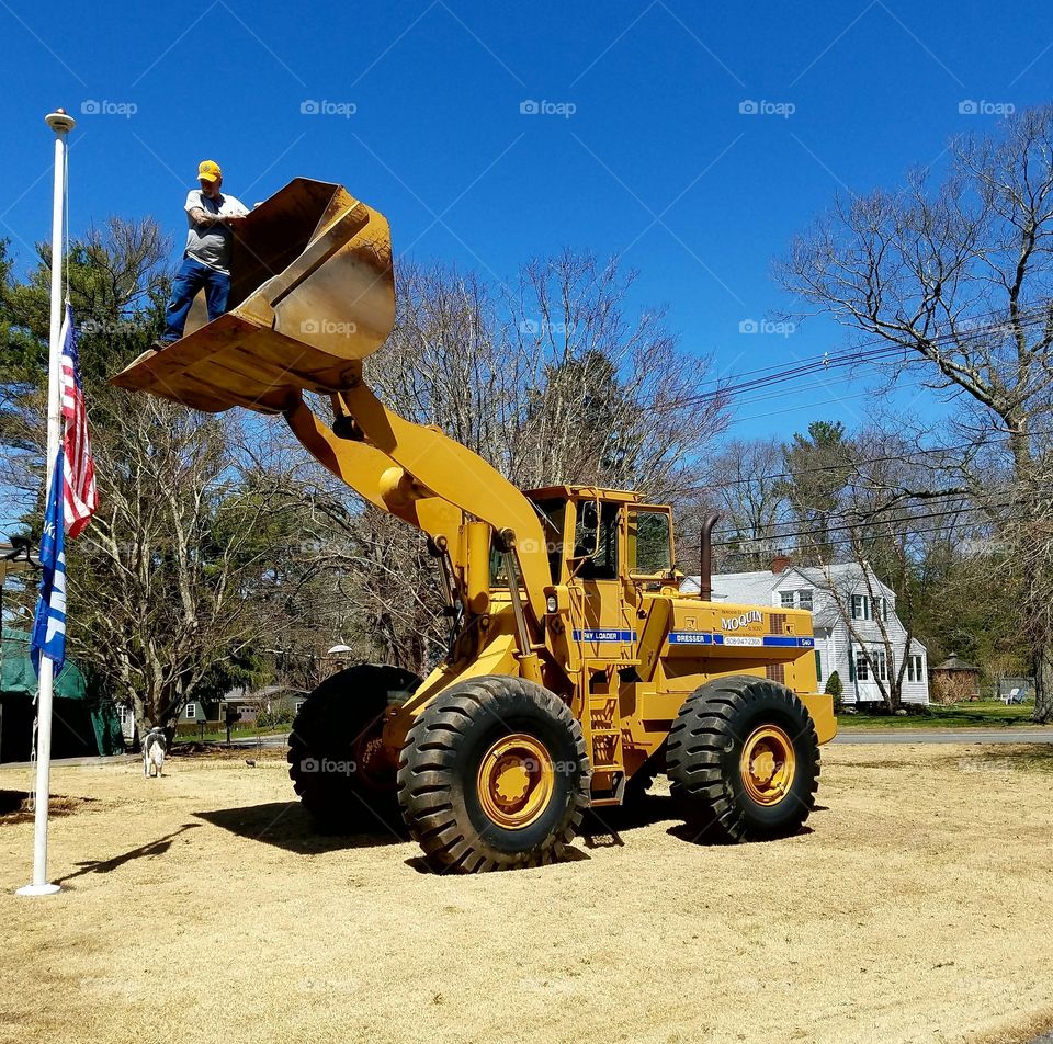 Worker in Bucket of Front End Loader🚜 lifting man up to reach top of flagpole  that needed a new topper.