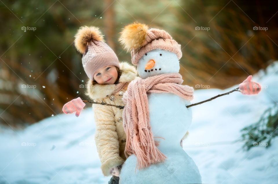 Little girl with snowman in winter park