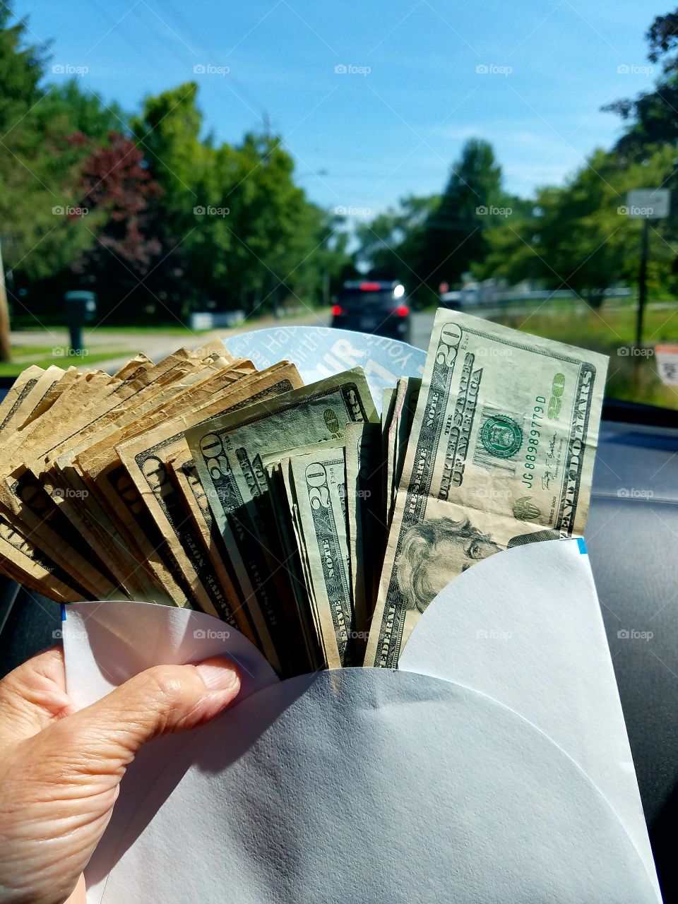 Holding envelope US $10 & $20 bills going down road in a car.