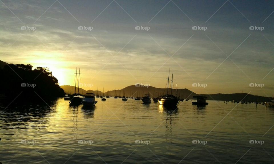 Céu amarelado ao entardecer sobre as águas do oceano com embarcações.