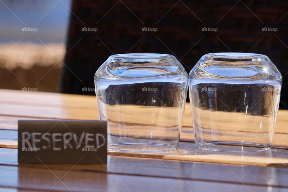 Outdoor wood restaurant patio table with Reserved sign and two crystal clear water glasses turned upside down, restaurant dining, food, summertime experiences 