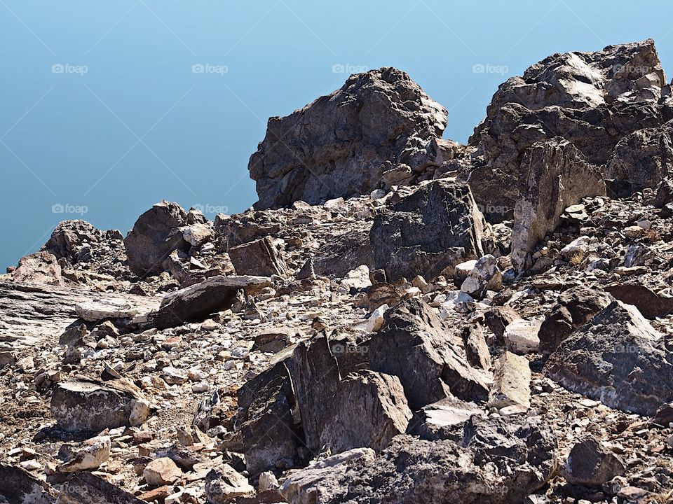 Jagged rocks and boulders along the shoreline of Ochoco Lake in Central Oregon on a sunny spring day.