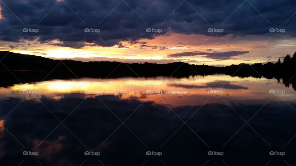 dark orange Sunset with dramatic clouds reflected in lake