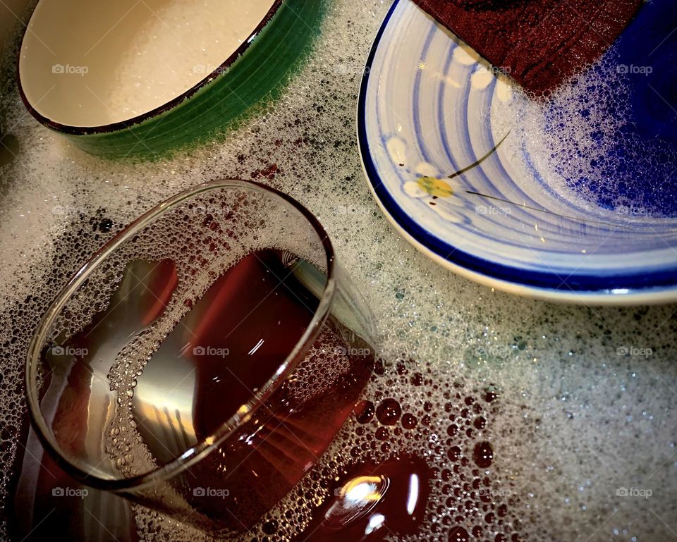 Dishes In Soap Water With Bubbles Seeing Through Clear Glass Cup A Fork That Seems To Be Three But Is One With Refraction And Reflection Through The Water.