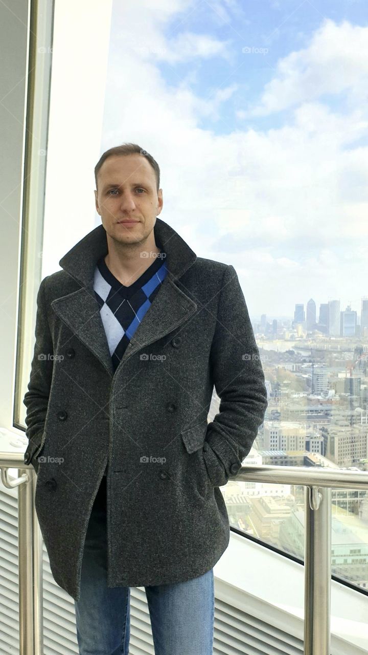 A handsome man stands by the window against the background of London business area