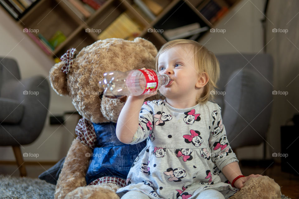 Baby girl drinking last drops of coca cola with teddy bear